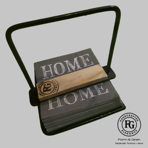 Form & Grain handcrafted napkin holder with black steel frame and spruce timber logo bar holding folded “Home” napkin